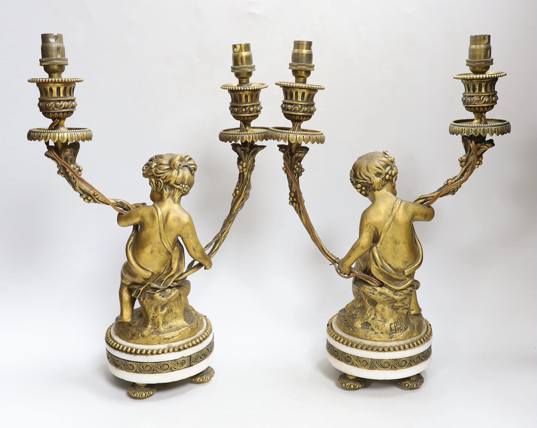 After Clodion (1738 –1814) Pair of two branch gilt bronze candlesticks in the form of Putti, each raised on circular bases, 34cm high